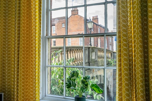 A room with a large window, yellow patterned curtains, and a potted plant on the windowsill.