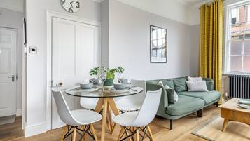 A modern living room with a round glass table, white chairs, a green sofa, and a framed picture on the wall.