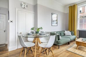 A modern living room with a round glass table, white chairs, a green sofa, and a framed picture on the wall. - A family retreat that sleeps 4 guests in 2 bedrooms (York)
