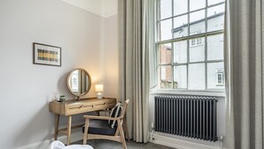 A hotel room with a bed, a desk with a chair, a mirror, a radiator, and a window with curtains. - A family retreat that sleeps 4 guests in 2 bedrooms (York)