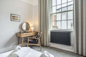 A hotel room with a bed, a desk with a chair, a mirror, a radiator, and a window with curtains. - A family retreat that sleeps 4 guests in 2 bedrooms (York)