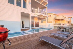 A modern two-story house with a wooden deck, a swimming pool, and outdoor furniture. - Explore "Coastal View" - New Custom Beach Home! (Inlet Beach)