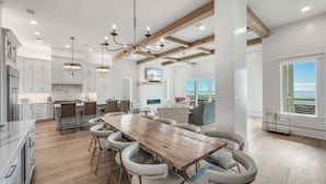 A spacious kitchen with a long wooden table and bar stools, white cabinetry, and a large island. - Coral Cay - A Stunning Home with Exquisite Views! (Inlet Beach)