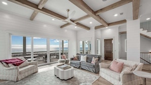 A spacious living room with a large window overlooking the ocean, a ceiling fan, and a cozy seating area with a sofa and armchairs. - Coral Cay - A Stunning Home with Exquisite Views! (Inlet Beach)