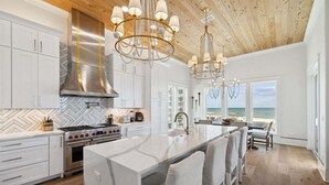 A modern kitchen with white cabinetry, a large island, and a view of the ocean. - Ultimate 8-Bedroom Getaway for Families & Groups (Inlet Beach)