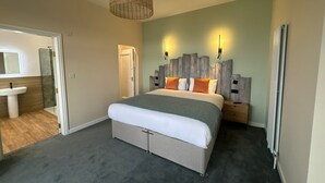 A bedroom with a bed, bedside tables, a hanging light fixture, a radiator, and a bathroom visible through an open door. - The Balmoral Hotel (Blackpool)