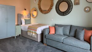 A bedroom with a bed, a grey sofa, and multiple wall mirrors. - The Balmoral Hotel (Blackpool)