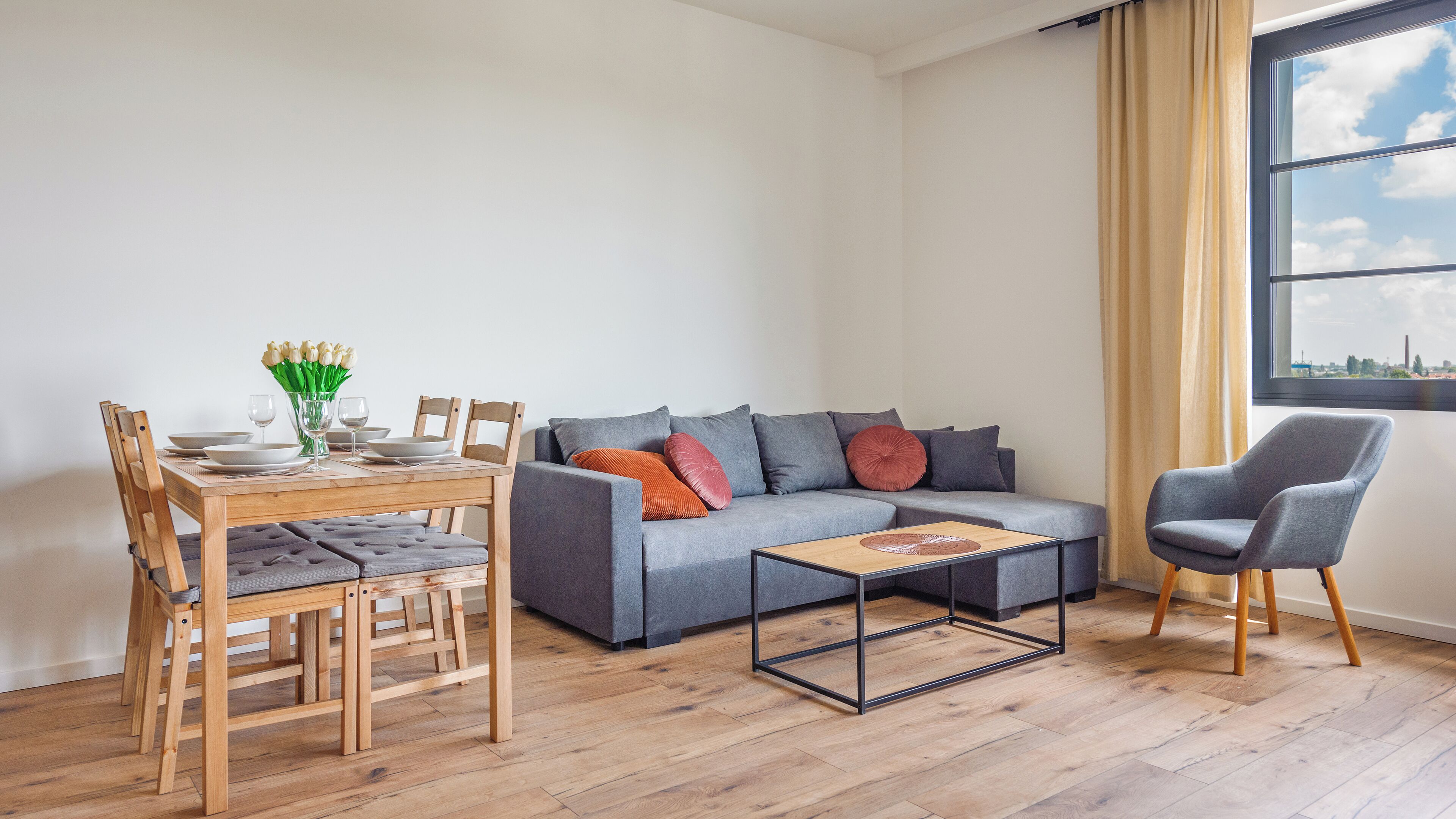 A modern living room with a grey sofa, wooden dining table, and chairs.