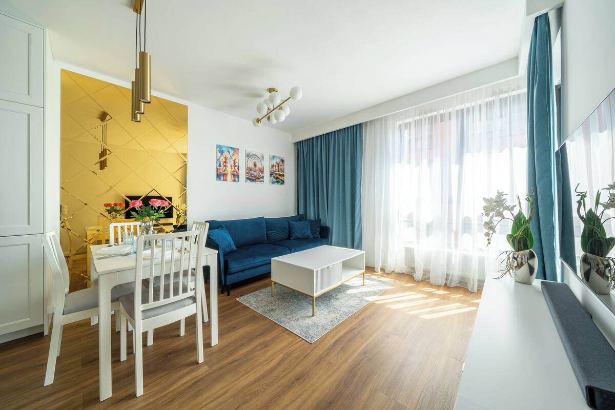 A modern living room with a blue sofa, white coffee table, and dining area with a white table and chairs.