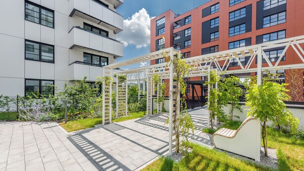 Un patio con una pérgola, zona de estar y abundante vegetación.