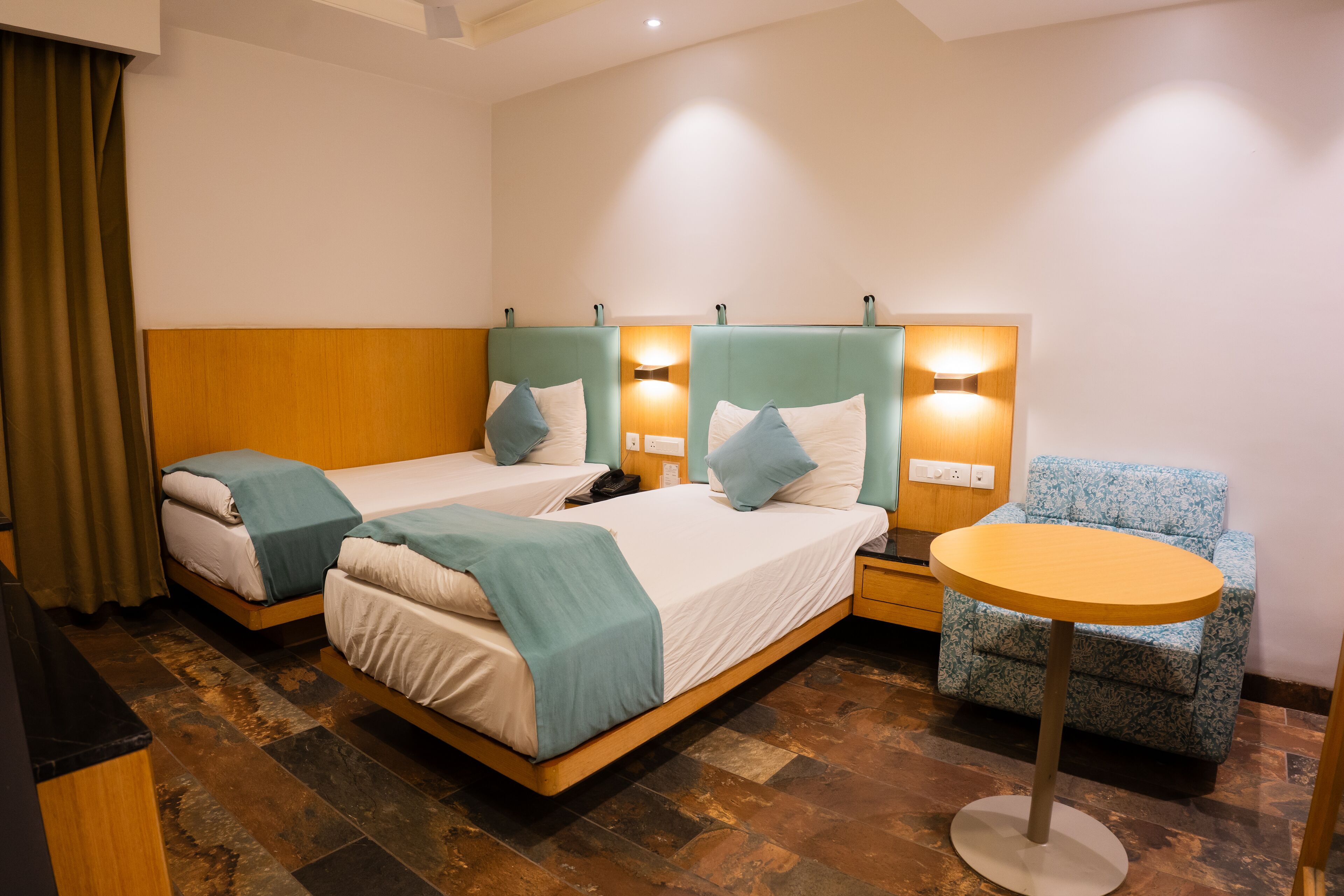 Habitación de hotel con dos camas individuales, una mesita redonda y un sillón estampado.