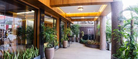 Un corredor interior amplio con grandes plantas en macetas, vigas de madera y un diseño arquitectónico moderno.