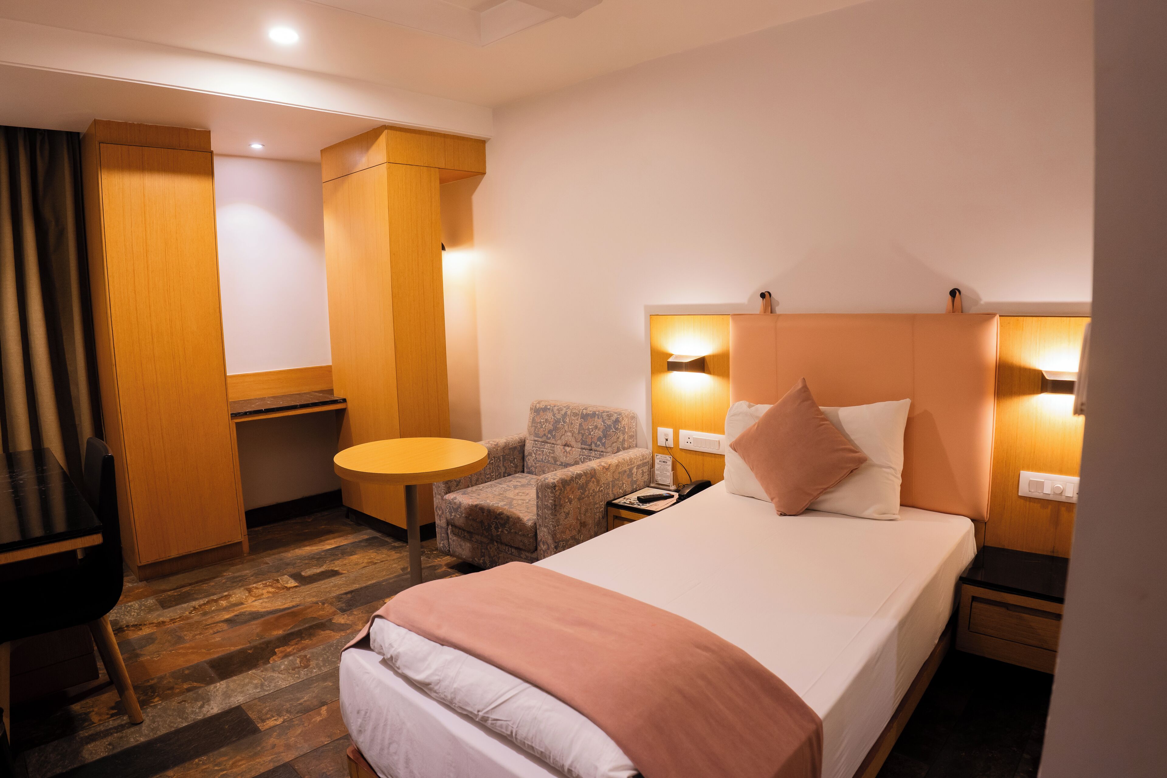 Quarto de hotel com uma cama, uma cadeira, uma mesinha e uma escrivaninha.