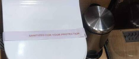 Un inodoro con tapa que muestra la etiqueta 'SANITIZED FOR YOUR PROTECTION'.