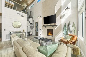 Amplia sala de estar con sofá, mesa de centro, chimenea, televisor y escalera que lleva a un nivel superior.