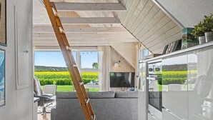 A modern interior with a wooden ceiling, a grey sofa, a TV, and a kitchen area.