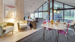 A spacious living area with a dining table, chairs, and a sofa. There is a poster on the wall and a guitar leaning against the wall.