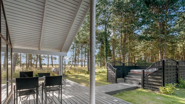 A covered outdoor area with a wooden deck, a table with chairs, and a view of a forested area.