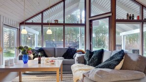 A cozy living room with a large window, a sofa, a table with a vase, and a rug.