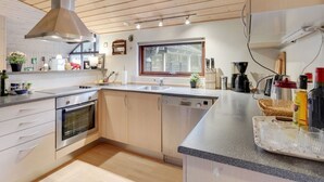 A modern kitchen with wooden cabinets, a stainless steel range hood, a built-in oven, and a large window providing natural light.