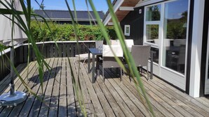 A wooden deck with outdoor furniture, a large sliding glass door, and a view of a house with a dark exterior and a tiled roof.