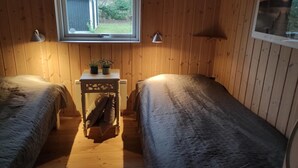 A cozy room with two beds, a small table with a plant, and a window overlooking a garden.