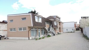 Un immeuble résidentiel à deux étages, avec un escalier menant à l’entrée, une allée pavée et un bâtiment blanc voisin.