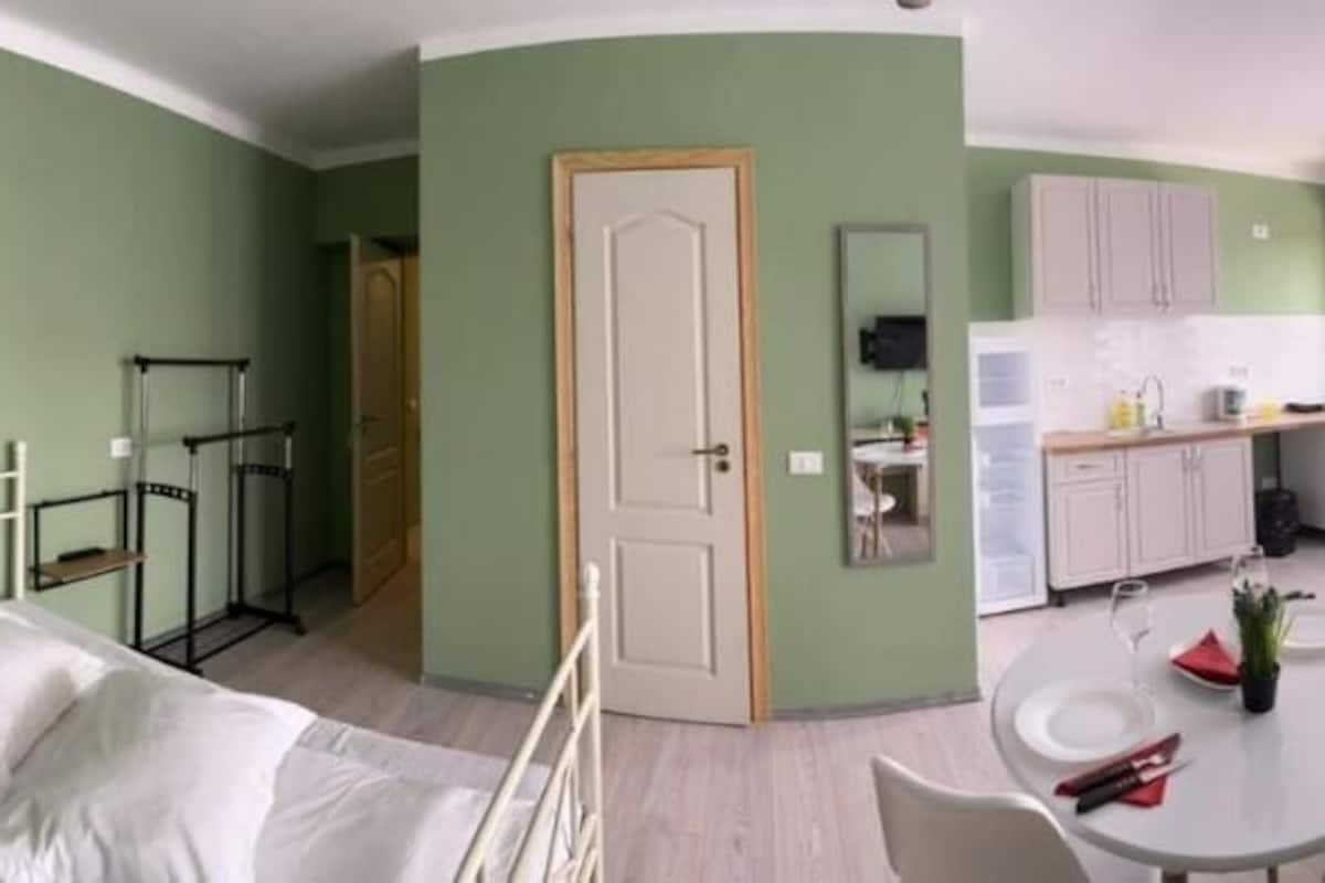 Una habitación con cama, una mesa de comedor con sillas, una zona de cocina y un televisor montado en la pared.