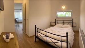 A bedroom with a bed, a window, a bedside table, and a chair in the background. - PREMONT STUDIOS GHIMBAV (Ghimbav)