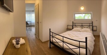 Un dormitorio con cama, ventana, mesita de noche y una silla al fondo.