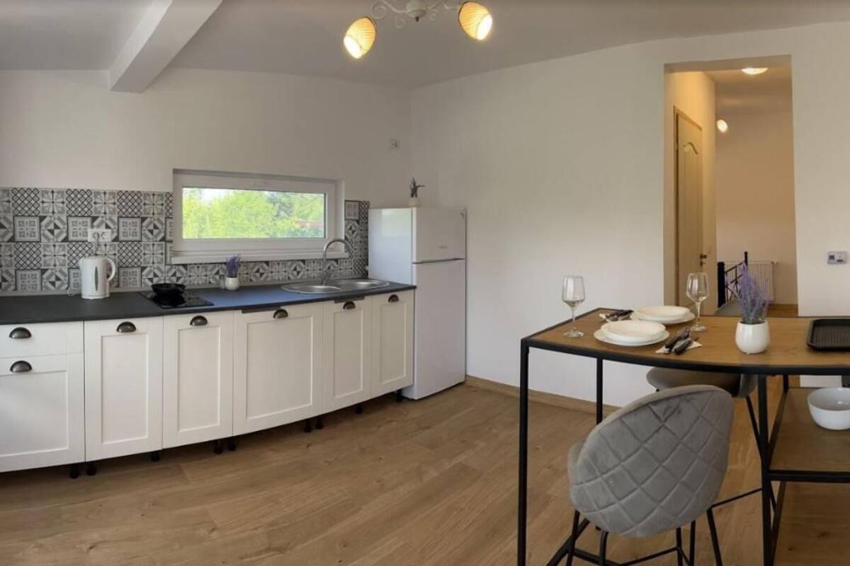 Cocina moderna con armarios blancos, encimera negra y una ventana. Hay una mesa de comedor con sillas y un florero con flores.