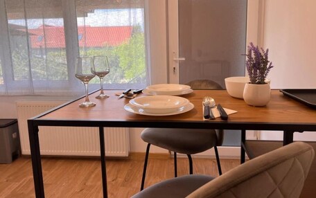 A dining area with a table set for two, two wine glasses, a plate, cutlery, and a potted plant.
