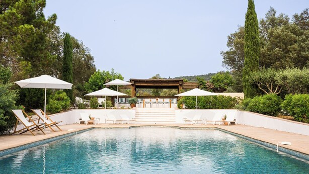 A rectangular pool with clear blue water, surrounded by white lounge chairs and umbrellas.