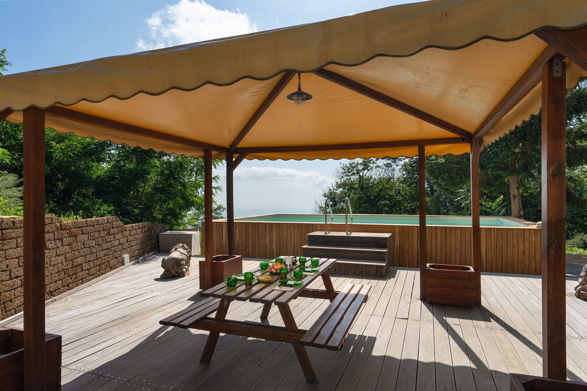 Un espacio al aire libre techado con piso de madera, una mesa de picnic y asientos.