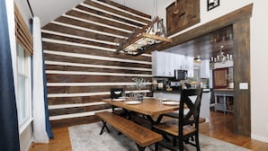 Un coin repas avec une table et des bancs en bois, un luminaire suspendu et une cuisine en arrière-plan.