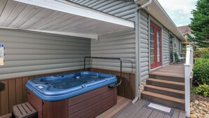 Un jacuzzi en una terraza de madera con escalones que conducen a una casa con puerta roja.