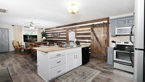 Una cocina con una puerta de madera estilo granero, armarios blancos, una isla grande y un horno empotrado.