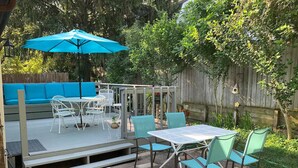 An outdoor patio with a covered seating area, a table with chairs, and a blue umbrella.