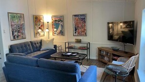 A living room with a blue sofa, a coffee table, a wicker chair, a TV, and wall art.