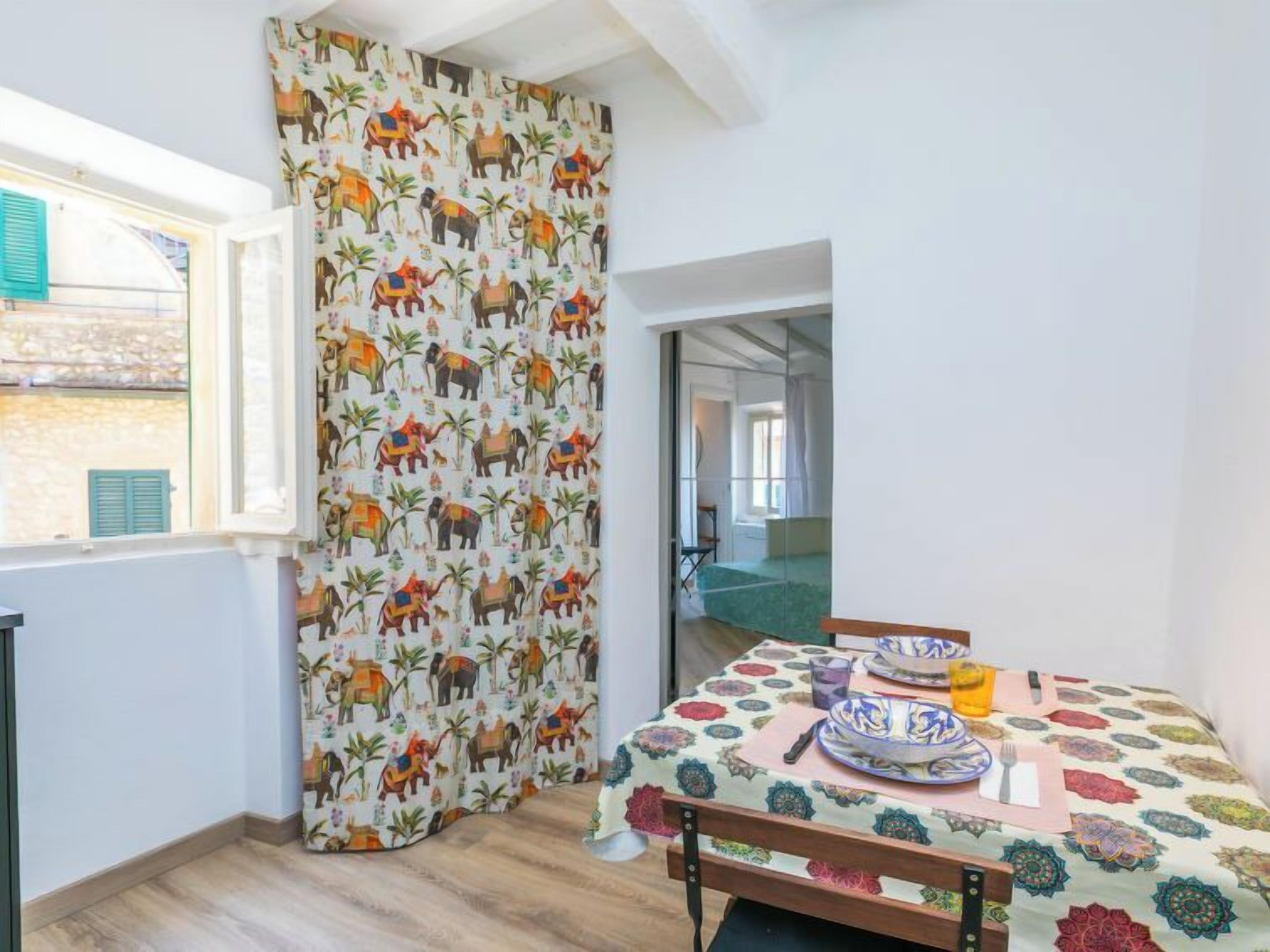 A room with a bed, a table set with plates and a glass, and a window with a view of a building outside.