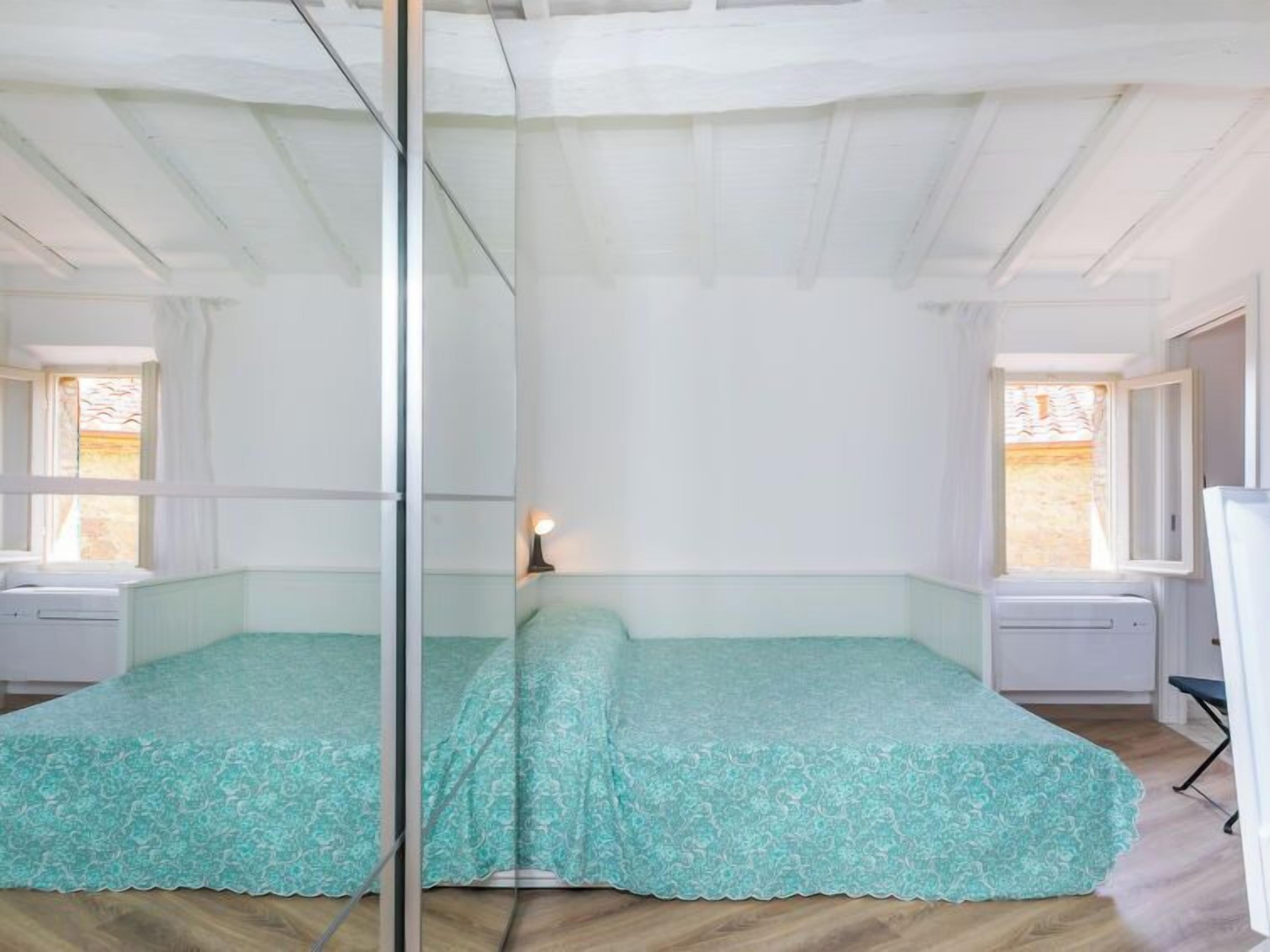 A room with two beds, a glass partition, and a window with curtains.