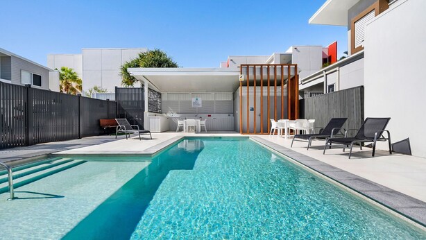 A modern outdoor pool area with clear blue water, surrounded by a black fence, and furnished with lounge chairs and tables. - Spirit of Allura - Located in the beautiful Coolum Beach (Coolum Beach)