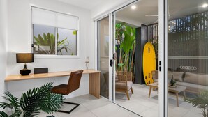 A modern living room with a glass door leading to a balcony, a desk with a lamp, a chair, and a surfboard. - Spirit of Allura - Located in the beautiful Coolum Beach (Coolum Beach)