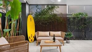 A modern outdoor seating area with wicker furniture, a yellow surfboard, and a wooden table with wine glasses and a bottle. - Spirit of Allura - Located in the beautiful Coolum Beach (Coolum Beach)
