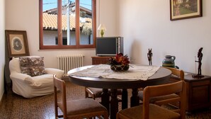 Ein gemütliches Wohnzimmer mit Esstisch, einer Couch, einem Fernseher und einem Fenster mit Blick auf ein Haus.