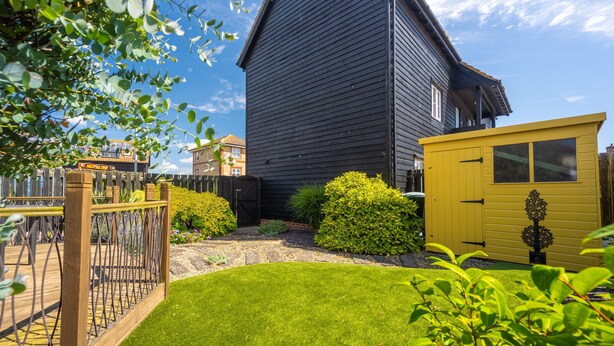 Una casa in legno scuro con tetto a falde, un cortile recintato e un piccolo capanno giallo.
