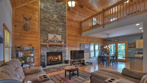 A spacious living room with a stone fireplace, wooden ceiling, and a cozy seating area. - Amber Sunsets dazzles with panoramic views, hot tub luxury, a custom firepit, screened porch, pool table, and pet-friendly hospitality! (Talking Rock)