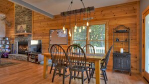 A cozy wooden interior with a fireplace, dining table, chairs, and a TV. - Amber Sunsets dazzles with panoramic views, hot tub luxury, a custom firepit, screened porch, pool table, and pet-friendly hospitality! (Talking Rock)