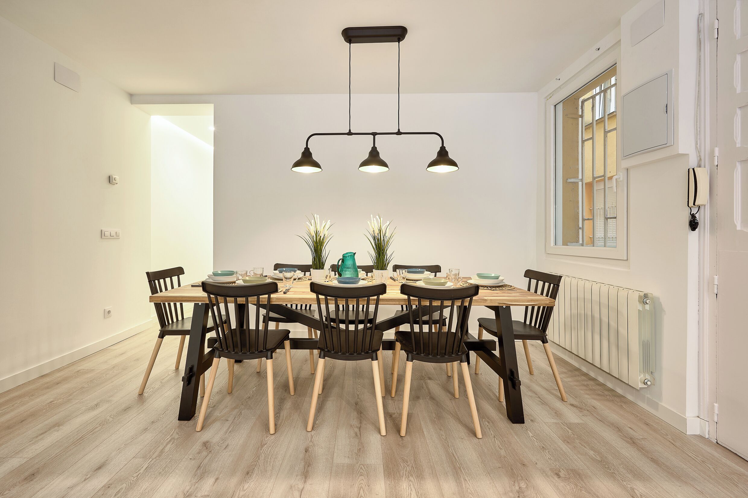 Een eetgedeelte met een houten tafel, zwarte stoelen en een hanglamp.