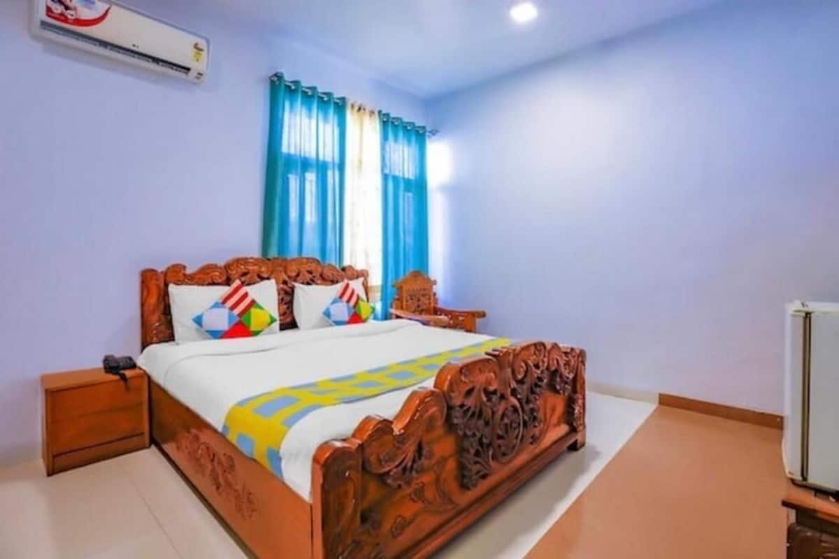 A bedroom with a wooden bed, a nightstand, a wall-mounted air conditioner, and a window with curtains.
